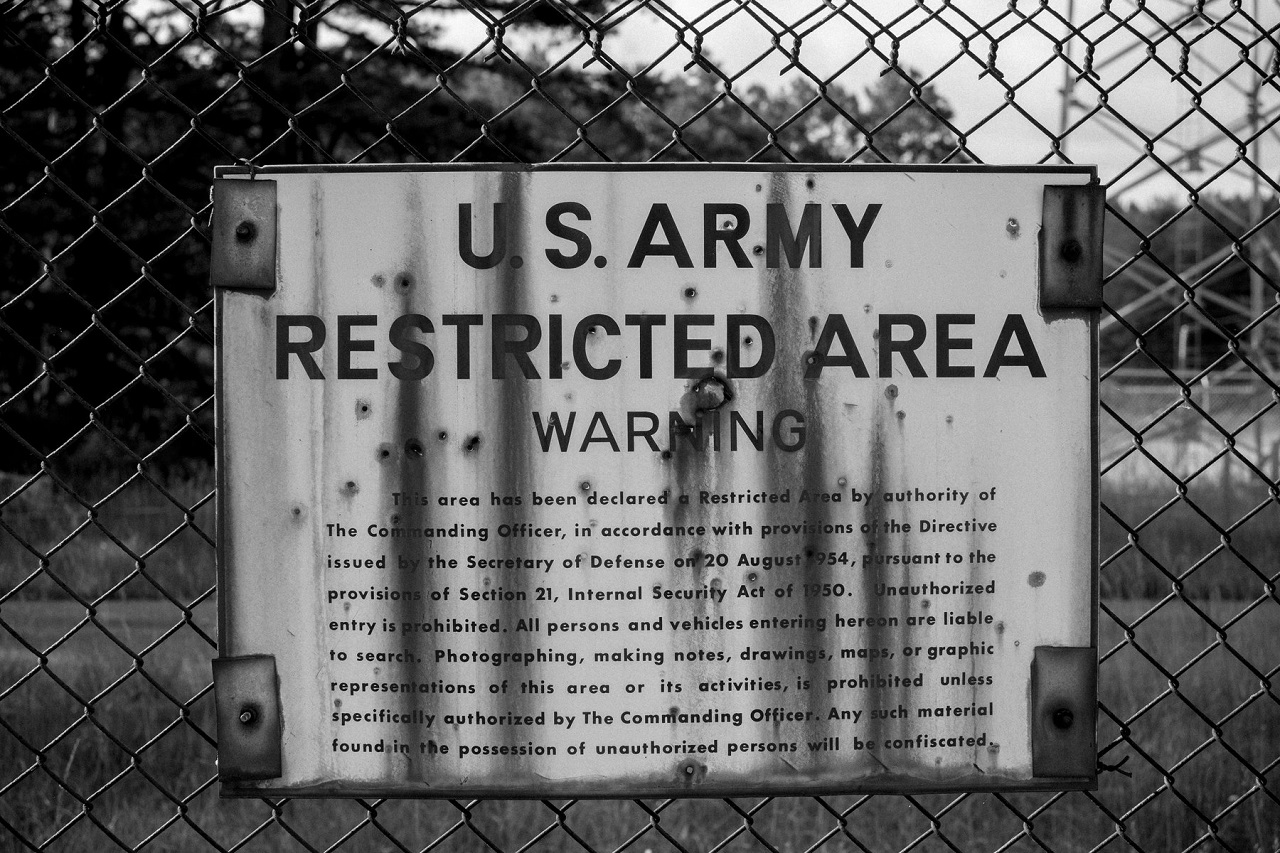 A U.S. Army restricted area warning sign on a rusting metal plate attached to a chain-link fence